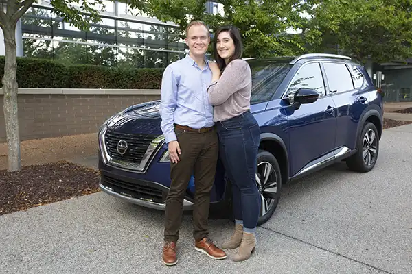 A couple pausing in front of a navy Nissan vehicle.