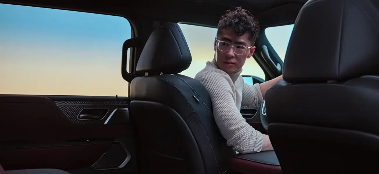 Tom hu in the front seat of a car twisted to look through the back window, the angle is from the rear passenger seat.