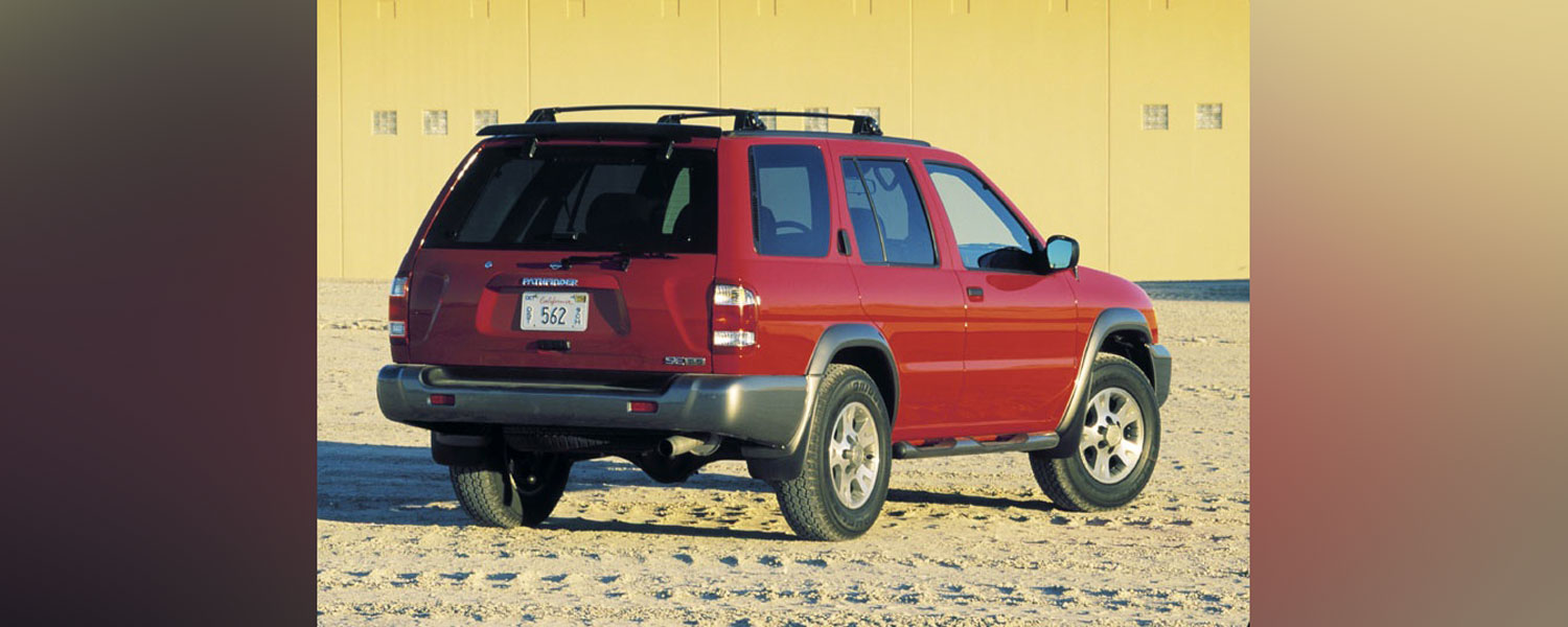 A red Nissan Pathfinder parked on a sandy beach with a yellow wall in the background.