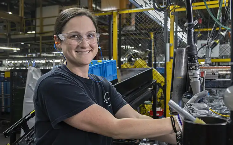 A woman with safety goggles in a factory smiling at the camera