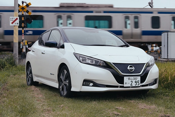 A white Nissan electric car parked in front of a moving train.