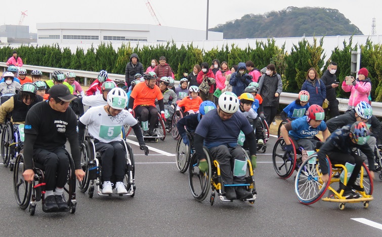日産追浜工場内グランドライブを会場に、車椅子でマラソンのスタートを切る参加者と応援の人々