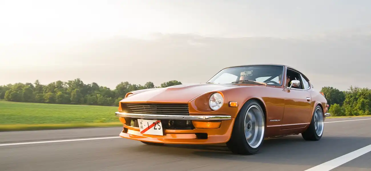 An orange classic Nissan Z driving on a road.