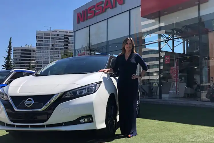 Una mujer parada junto a un Nissan LEAF blanco.