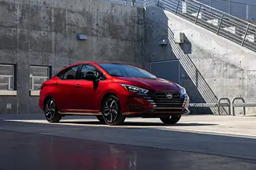 A red Nissan Versa parked at a concrete building