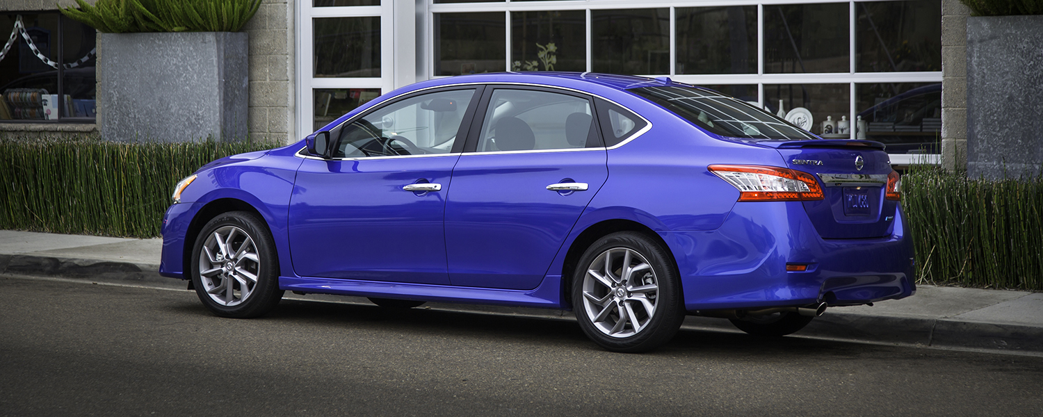 A blue Nissan Sentra parked in front of a building