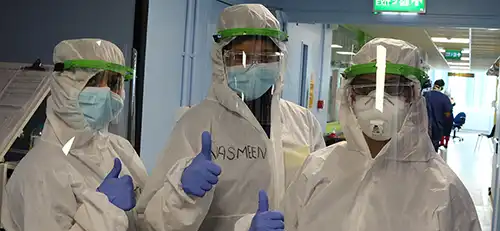 Three people in hazmat suits and medical masks standing in hospital