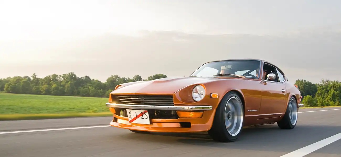 An orange classic Nissan Z driving on a road.