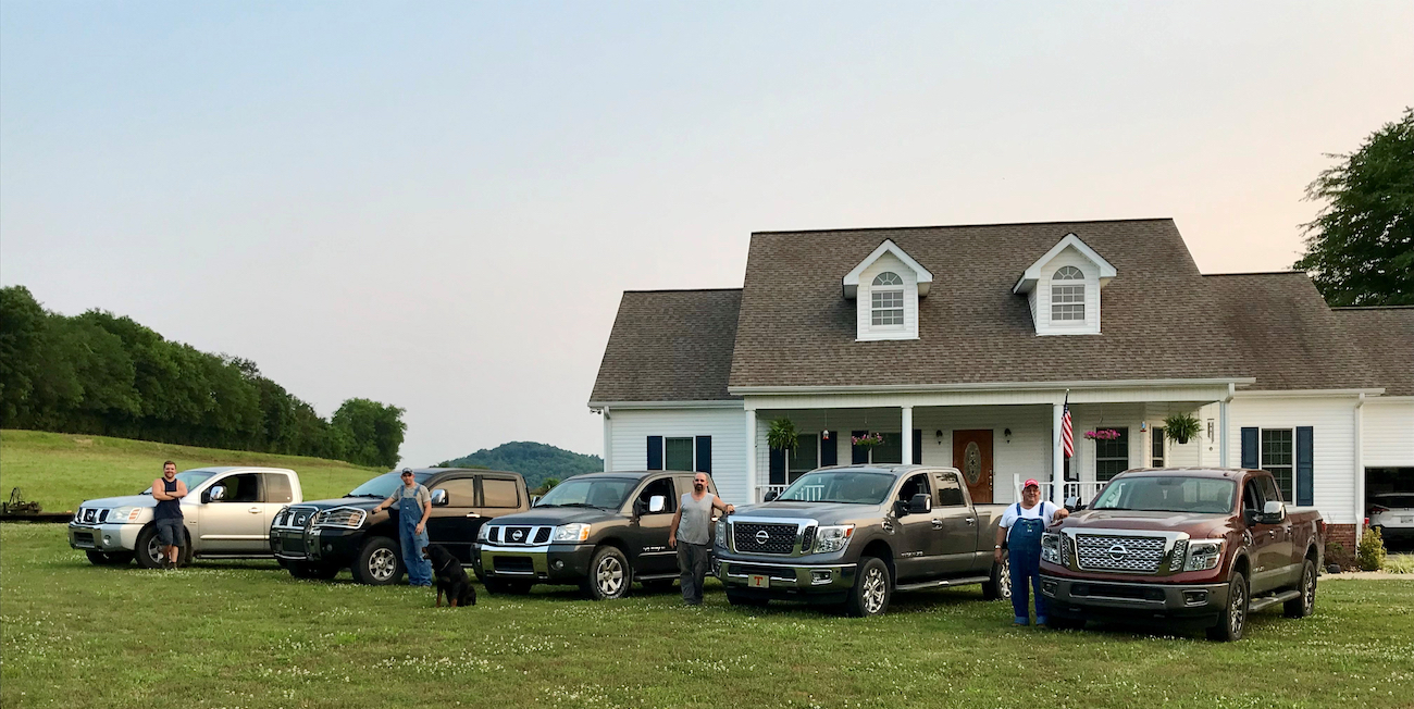 5 trucks, 5 people, and a dog pausing in front of a white house.