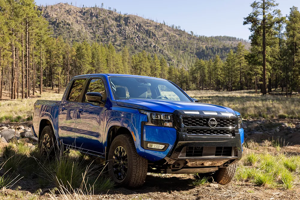 Front right 3/4 view of the 2027 Nissan Frontier Sport Edition parked on a clearing in a wooded area.
