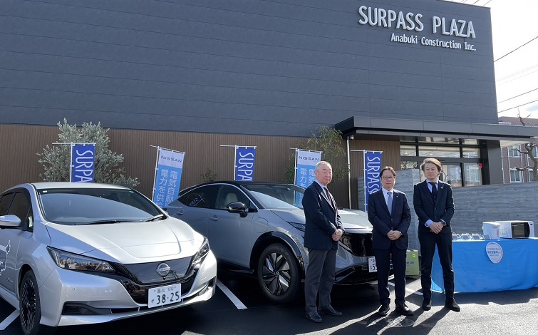 マンションモデルルーム前で電気自動車とともに記念撮影する穴吹工務店、日産自動車、日産プリンス香川販売の代表者（男性３名）