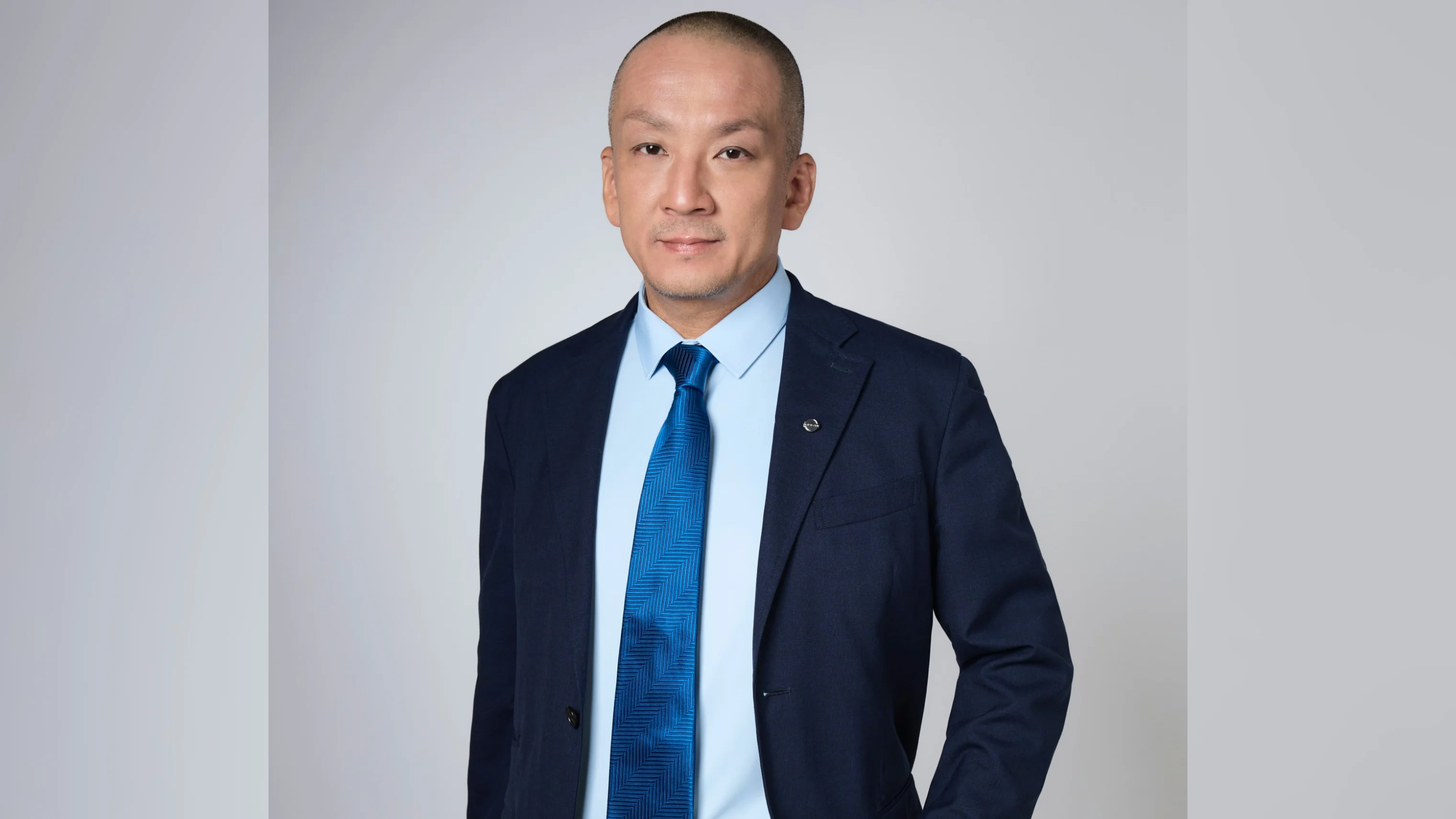 A photo of Yoshinori Kanazawa wearing a a black suit with a dark blue bow tie