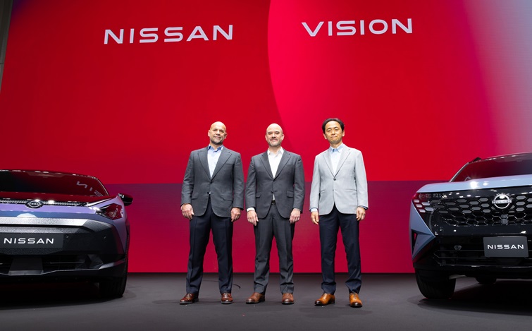 赤い背景のステージ上で、3人の人物が正面を向いて並んで立っており、左右には日産の車両が正面向きに配置されている。背景には「NISSAN」「VISION」の文字が表示されている。