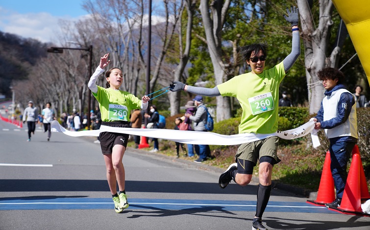 A male runner and a female escort runner reaching the finish line (both wearing yellow-green shirts)