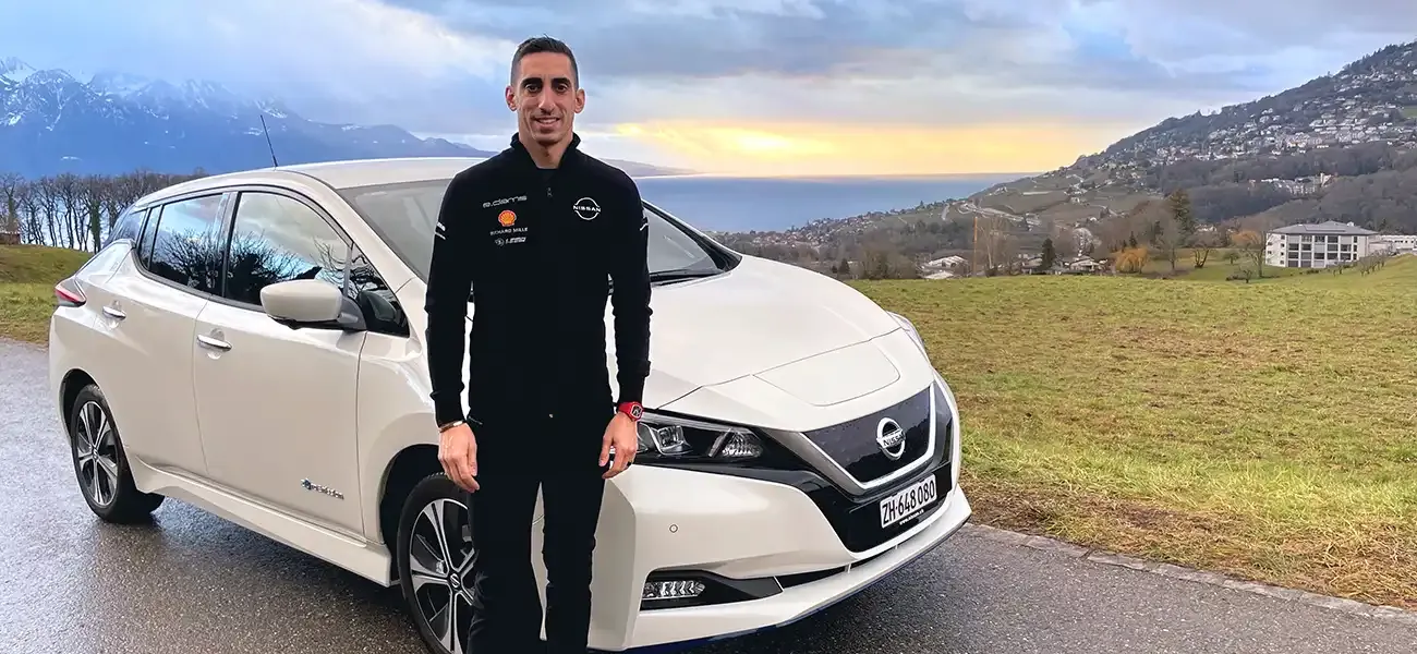 Sébastien Buemi pausing in front of a white Nissan LEAF.