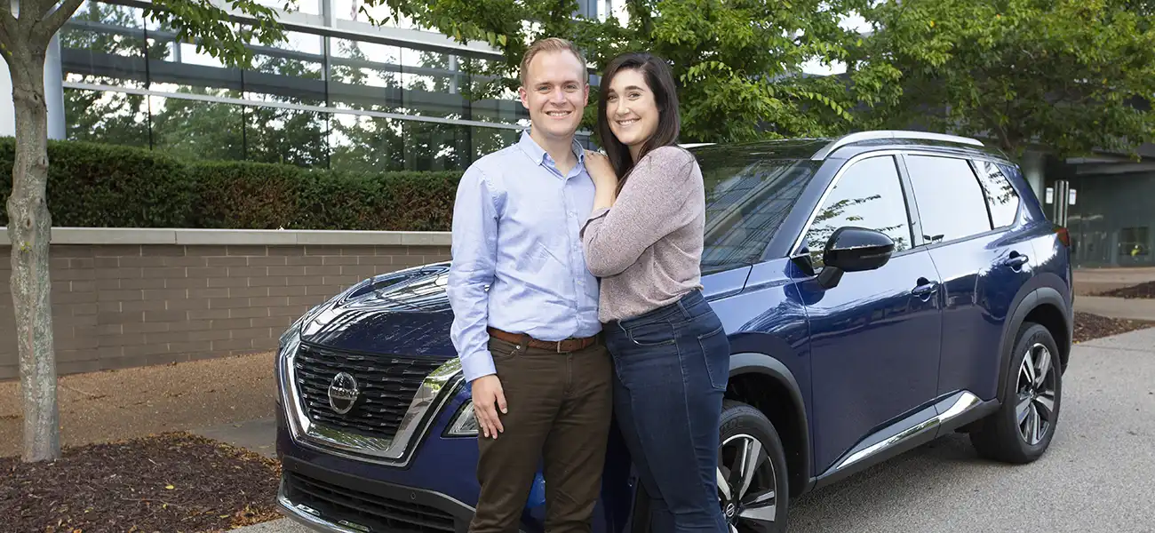 A couple pausing in front of a navy Nissan vehicle.