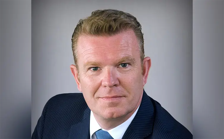 Christian from the shoulders up in a blue pin stripe suit and blue tie, smiling.