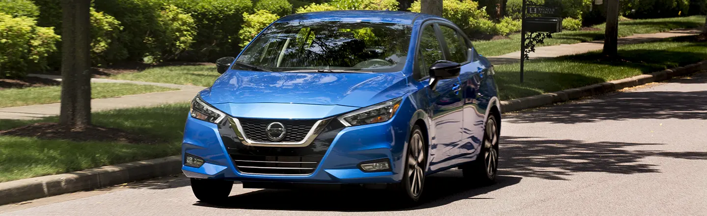 Front view of a blue 2021 Nissan Versa driving in a neighborhood road.