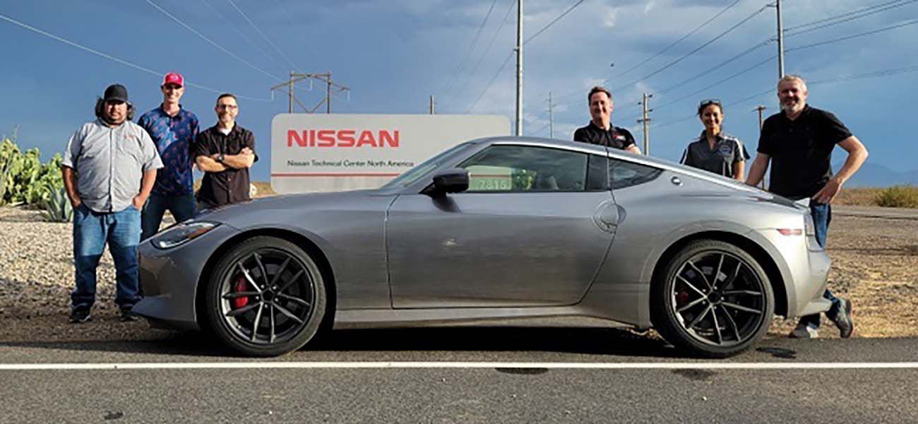 6 people standing by a silver Nissan Z.