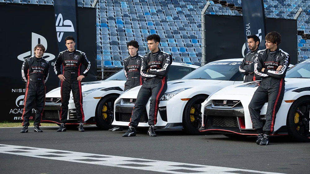 Gran turismo drivers in black, white and red racing suits leaning on white racing GT-Rs on a racetrack.