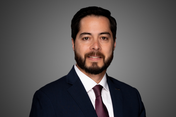 Leo smiling in a blue suit and red tie form the mid arms up.