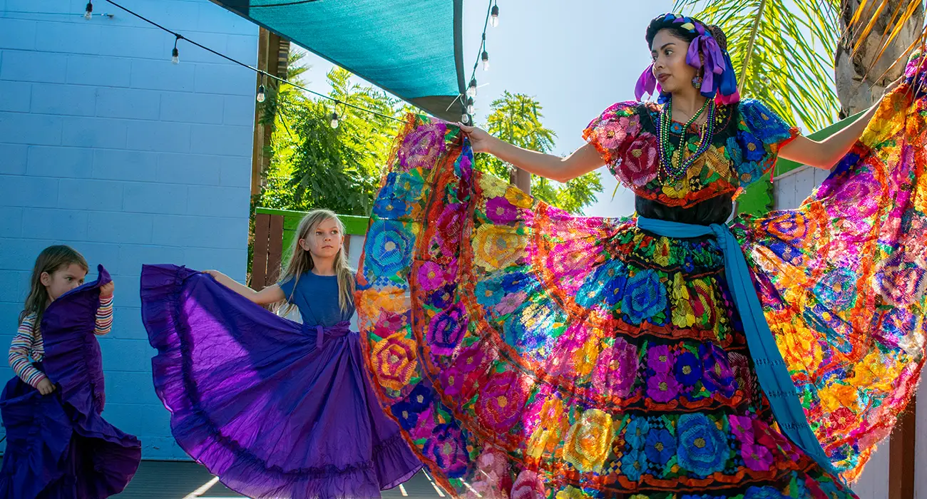 A dancing woman in a colorful dress with the sun shining through the colors with two children on her side