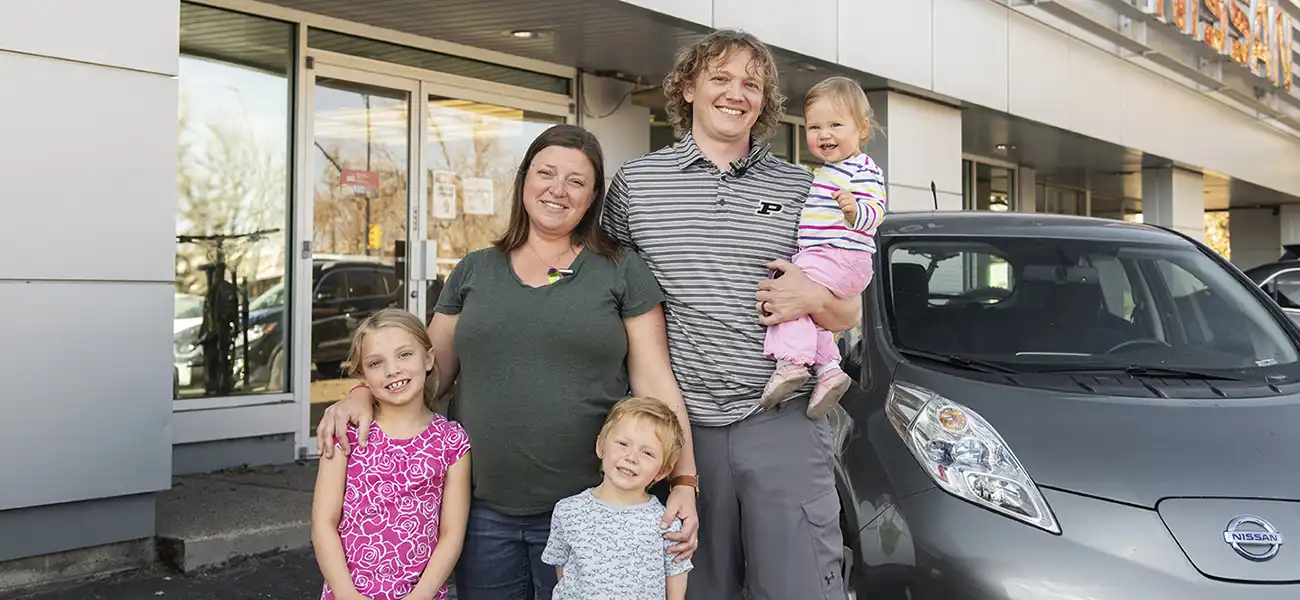 A family of 5 standing next to their gray Nissan LEAF.