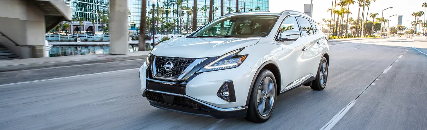A white 2024 Nissan Murano driving down a city road with palm trees and buildings in the background