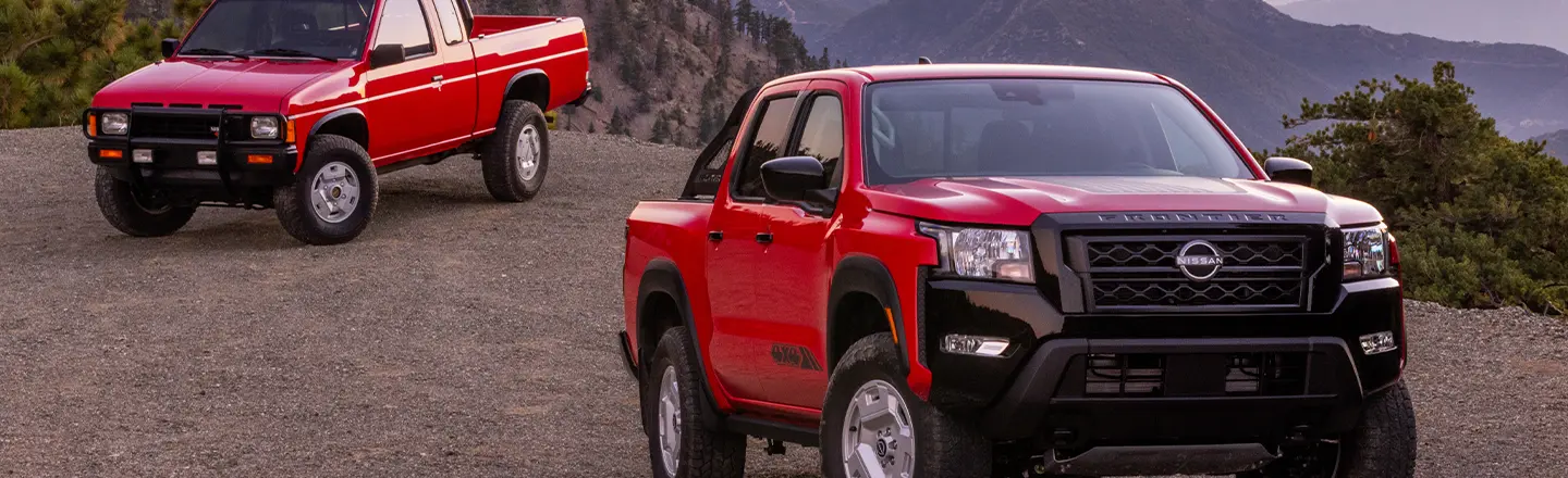 An original Nissan Frontier Hardbody from the 80s parked in the background and the 2024 Nissan Frontier Hardbody parked in the foreground with both front grilles showing
