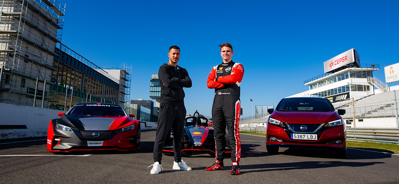 2 hombres posando delante de los coches Nissan en la pista de carreras.