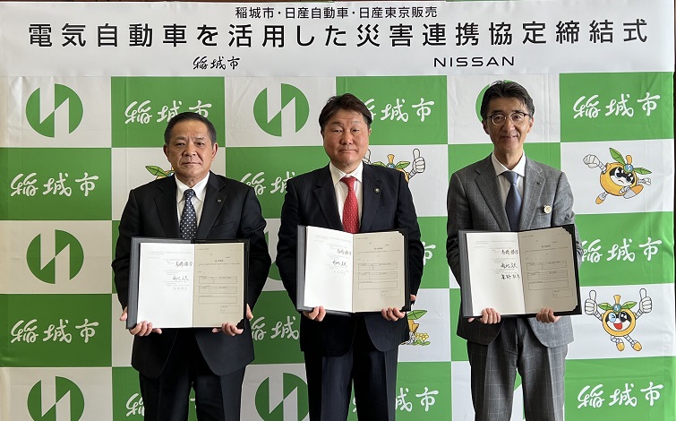 協定書を手に記念写真を撮る、稲城市、日産自動車、日産東京販売それぞれの代表者（いずれもスーツ姿の男性）