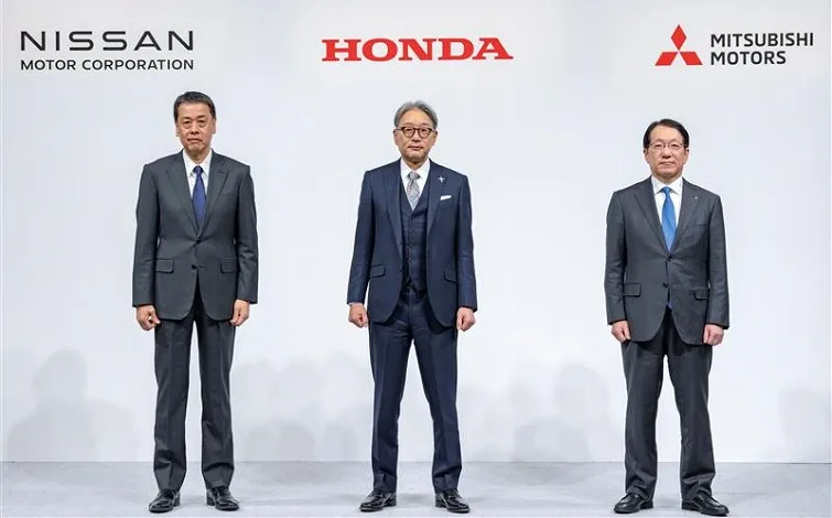 Three representatives standing facing forward with company logos in the background (from left to right): Makoto Uchida (Nissan Motors), Toshihiro Mibe(Honda), and Takao Kato (Mitsubishi Motors). They are wearing dark suits with ties.