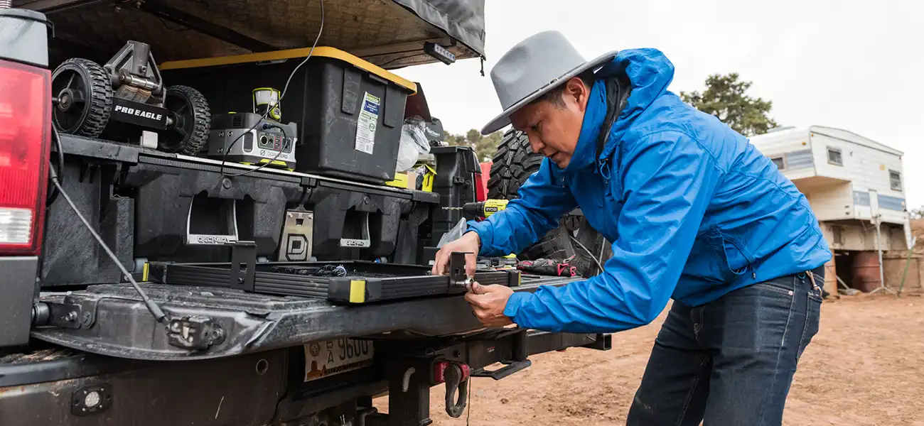A man in a blue jacket is working on the back of a truck.