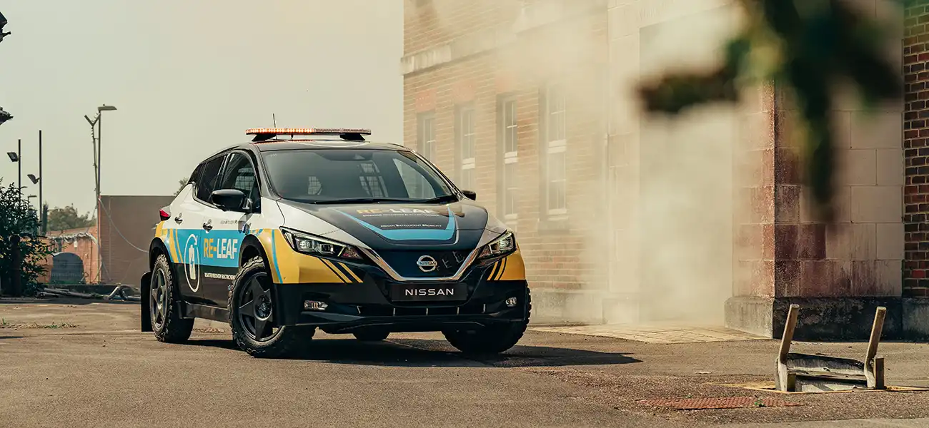 A Nissan LEAF parked next to a smokey building.