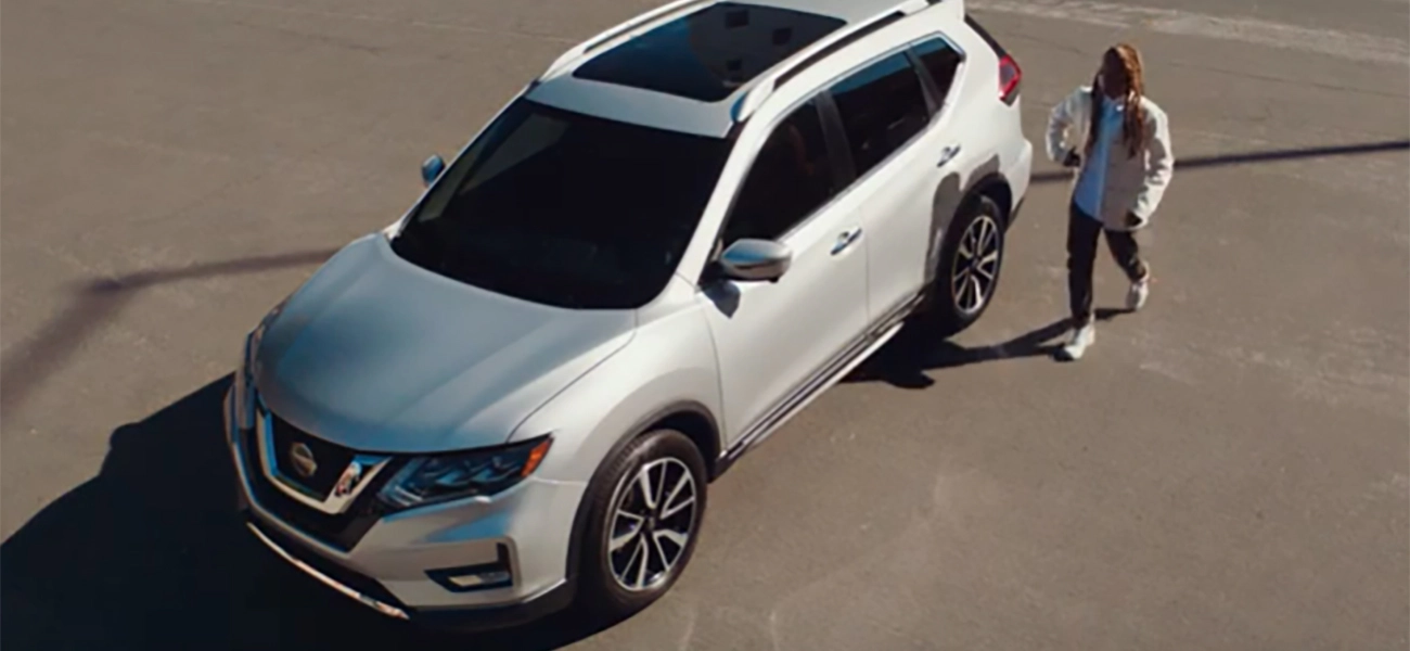 A person walking towards a silver Nissan Rogue in a parking lot.